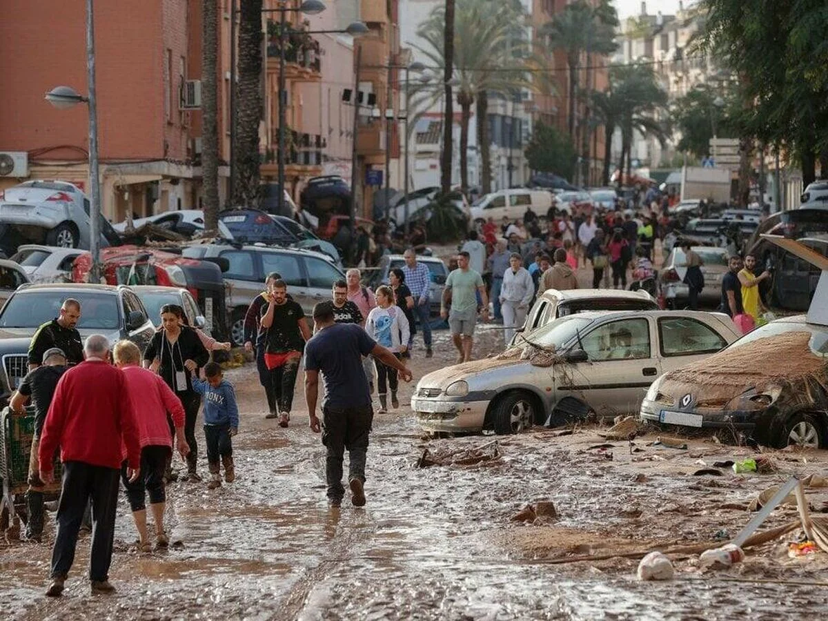 Fuente: EFE. Fotografía de una calle de Valencia llena de lodo y de coches en mal estado, junto a personas afectadas y voluntarias.